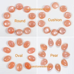 May include: A collection of sunstone cabochons in various shapes, including round, cushion, oval, and pear. The stones are a light peach colour with a shimmery, iridescent finish.