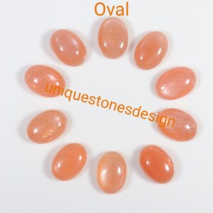 May include: Ten oval-shaped sunstone cabochons in various shades of orange. The stones are arranged in a circle on a white background. The text "uniquestonesdesign" is visible in the centre of the circle.