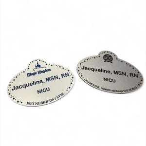 May include: Two oval name badges. One is off-white with blue text: "Magic Kingdom Jacqueline, MSN, RN NICU BEST NURSES' DAY EVER." The other is silver with black text: "Jacqueline, MSN, RN NICU CELEBRATING NURSES AROUND THE WORLD."