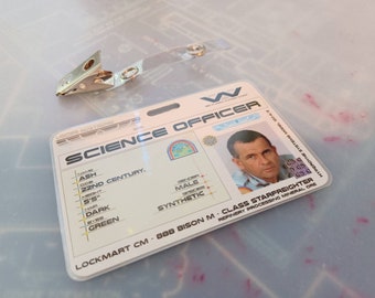 May include: A white plastic ID card with the text "SCIENCE OFFICER" in black. The card has a photo of a man with short brown hair and a beard. The text "LOCKMART CM 88B BISON M-CLASS STARFREIGHTER" is printed on the card.
