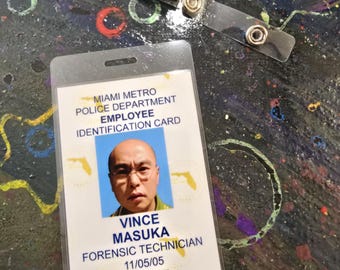 May include: Miami Metro Police Department employee identification card with a photo of Vince Masuka, Forensic Technician. The card is in a clear plastic holder, with a metal clip.