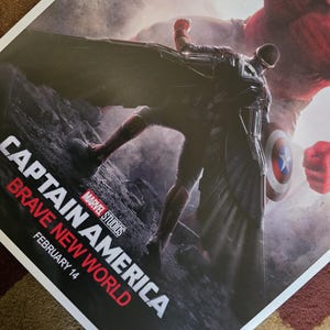 Op de afbeelding: Een filmposter voor Captain America: Brave New World, een productie van Marvel Studios. De poster toont Captain America in een zwart en rood pak, staande op een rotsachtig oppervlak. Hij staat tegenover een groot, rood, mensachtig figuur. De tekst "Captain America: Brave New World" is in rood en wit, met de releasedatum "14 februari" eronder.