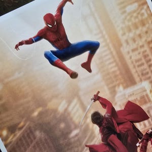 K&ouml;nnte beinhalten: Ein Druck, der Spider-Man in einem roten und blauen Anzug in einer dynamischen Pose zeigt, der ein Netz schie&szlig;t. Darunter k&auml;mpfen Figuren in roten Outfits mit Schwertern vor einem verschwommenen Stadtbild.