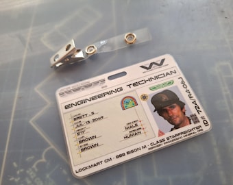 Puede incluir: Una tarjeta de identificación de plástico blanca con el texto "ENGINEERING TECHNICIAN" y "W" para Weyland-Yutani Corporation. La tarjeta tiene una foto de un hombre con una gorra negra y una etiqueta de nombre que dice "BRETT.S". La tarjeta también incluye el texto "LOCKMART CM 888 BISON M-CLASS STARFREIGHTER" y "ID# 724/R4-06J".