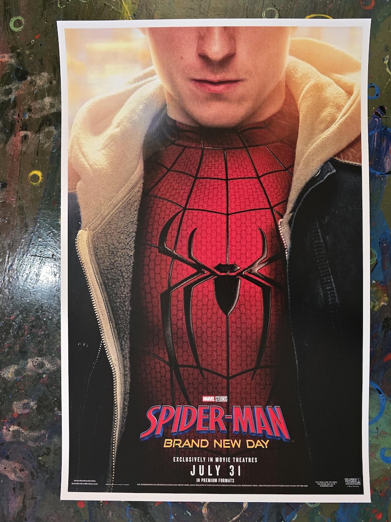 May include: A movie poster featuring a person wearing a red and black Spider-Man suit under a beige hoodie and dark jacket. The text reads Spider-Man Brand New Day, Marvel Studios, Exclusively in Movie Theatres, July 31, in Premium Formats.