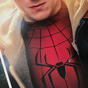 May include: A red and black Spider-Man costume top featuring a textured web pattern and a large black spider emblem on the chest, worn underneath a beige hooded jacket with a dark zipper and a visible fleece-lined interior texture.