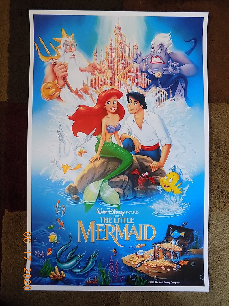 May include: A vintage movie poster for the Disney film "The Little Mermaid". The poster features Ariel, the mermaid princess, with her human prince, Eric. King Triton, Ursula the sea witch, and Flounder are also featured on the poster. The poster is set against a blue background with a castle in the background.