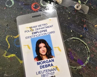 May include: A Miami Metro Police Department employee identification card with a photo of a woman with brown hair. The card reads "Morgan Debra Lieutenant 08/27/07".
