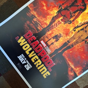 May include: A film poster for the movie "Deadpool & Wolverine" featuring the Marvel Studios logo. The poster shows Deadpool and Wolverine standing in a fiery landscape. The text "Only in Theaters July 26" is at the bottom of the poster.