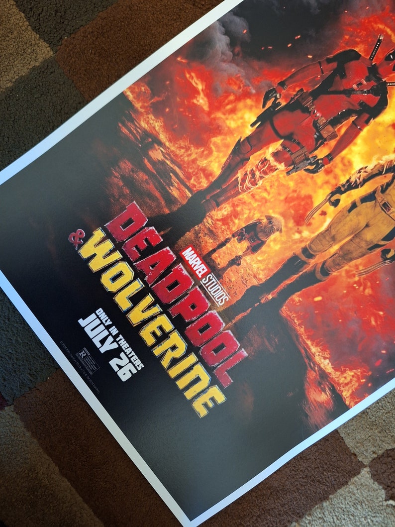 May include: A film poster for the movie "Deadpool & Wolverine" featuring the Marvel Studios logo. The poster shows Deadpool and Wolverine standing in a fiery landscape. The text "Only in Theaters July 26" is at the bottom of the poster.
