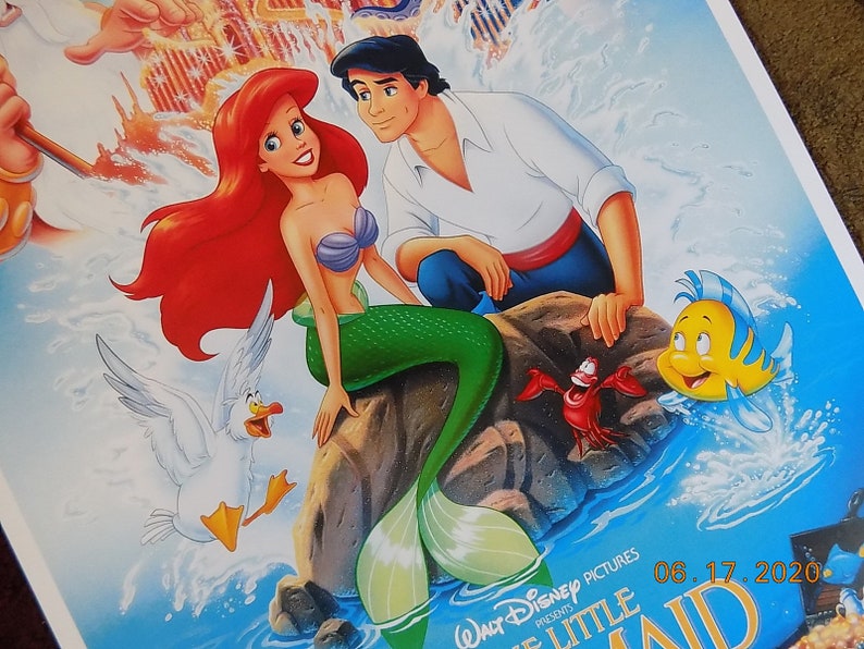 May include: A poster for the Disney movie The Little Mermaid featuring Ariel, a red-haired mermaid, and Prince Eric, a human prince. Ariel is sitting on a rock with her tail in the water, while Eric is standing behind her. The poster also features a seagull, a crab, and a yellow fish.