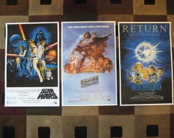 May include: Three movie posters for the Star Wars franchise. The posters are for Star Wars: Episode IV - A New Hope, Star Wars: Episode V - The Empire Strikes Back, and Star Wars: Episode VI - Return of the Jedi. The posters are all in the same style, with a white background and a black border. The posters feature images of the main characters from the films, as well as the title of the film and the tagline.