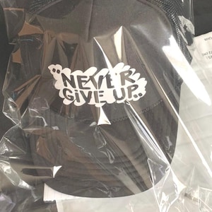May include: A black mesh trucker hat with a white embroidered design that says "NEVER GIVE UP."