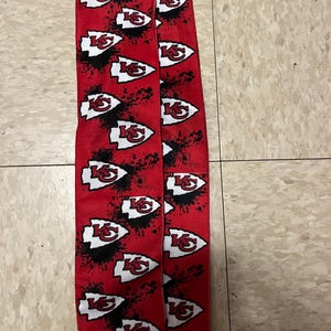 K&ouml;nnte beinhalten: Ein Paar rot-schwarze Socken mit einem wei&szlig;en Kansas City Chiefs-Logo, das sich auf dem Stoff wiederholt. Die Socken haben ein Spr&uuml;hfarben-Design.