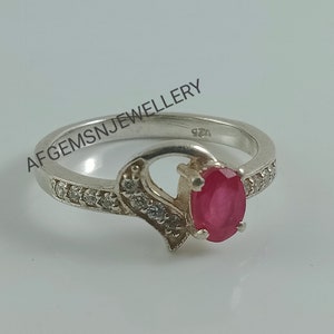 May include: A silver ring with a red oval gemstone and small clear stones set in the band. The ring is marked "925" on the inside.