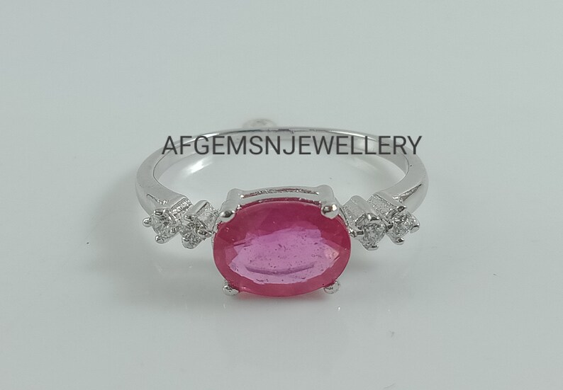 K&ouml;nnte beinhalten: Ein silberner Ring mit einem gro&szlig;en ovalen rosafarbenen Edelstein, umgeben von kleineren klaren Edelsteinen. Der Ring liegt auf einem wei&szlig;en Hintergrund. Der Text 'AFGEMSNJEWELLERY' ist auf dem Hintergrund gedruckt.