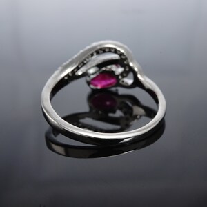 May include: A silver ring featuring a red gemstone and small clear stones. The ring is set in a delicate, intricate design.