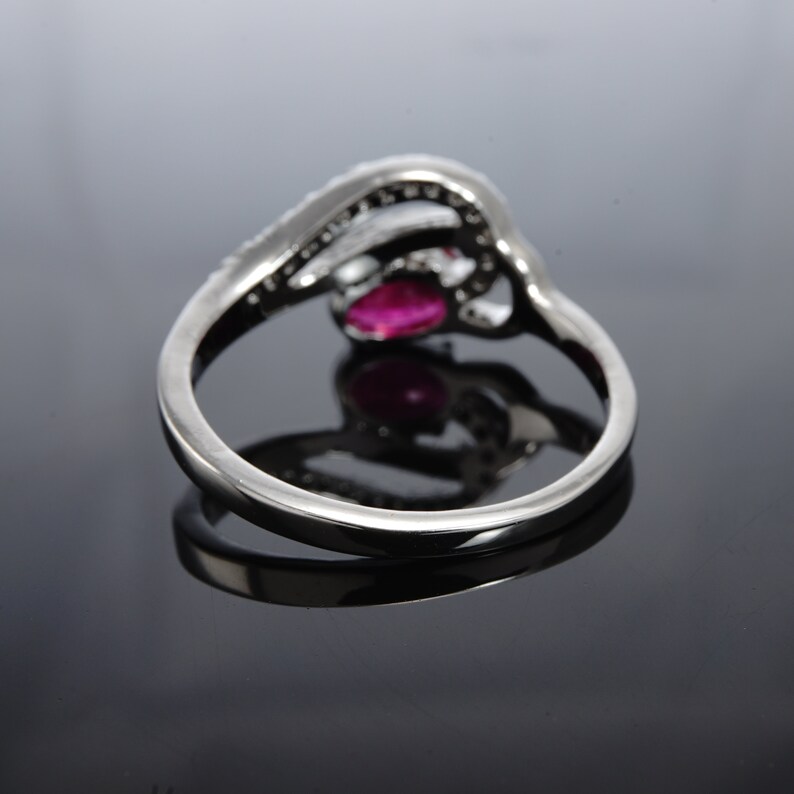 May include: A silver ring featuring a red gemstone and small clear stones. The ring is set in a delicate, intricate design.