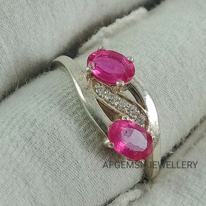 May include: A silver ring with two pink oval gemstones and a row of smaller clear gemstones. The ring is on a white fabric background. The text "AFGEMSJWELLERY" is visible in the bottom right corner of the image.