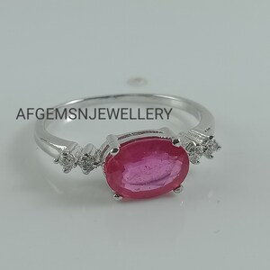 K&ouml;nnte beinhalten: Ein silberner Ring mit einem gro&szlig;en ovalen rosafarbenen Edelstein und kleineren klaren Edelsteinen auf der Ringschiene. Der Ring liegt auf einem wei&szlig;en Hintergrund. Der Text 'AFGEMSNJEWELLERY' ist auf dem Hintergrund gedruckt.