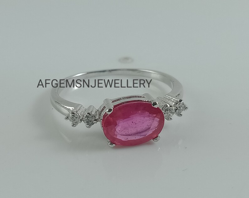 K&ouml;nnte beinhalten: Ein silberner Ring mit einem gro&szlig;en ovalen rosafarbenen Edelstein und kleineren klaren Edelsteinen auf der Ringschiene. Der Ring liegt auf einem wei&szlig;en Hintergrund. Der Text 'AFGEMSNJEWELLERY' ist auf dem Hintergrund gedruckt.
