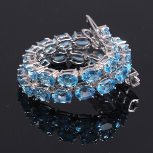 May include: A silver bracelet with a double row of oval-shaped blue gemstones. The bracelet has a clasp closure.