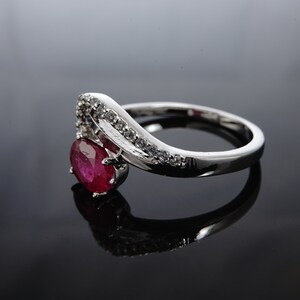 May include: A silver ring featuring a large oval ruby gemstone and smaller clear gemstones set in a curved band.