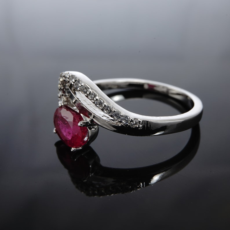 May include: A silver ring featuring a large oval ruby gemstone and smaller clear gemstones set in a curved band.