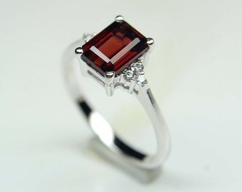 May include: A silver ring with a red gemstone and small clear gemstones around it.