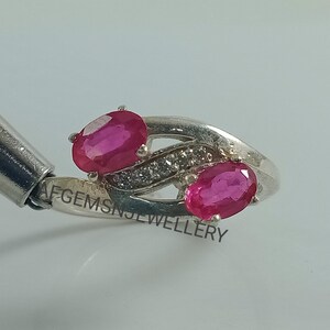 May include: A silver ring with two oval-shaped pink gemstones and a row of smaller white gemstones. The ring is engraved with the text "AFGEMS JEWELLERY".