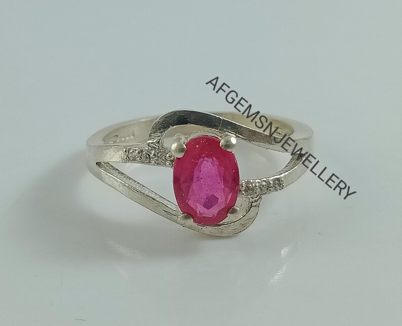 Puede incluir: Un anillo de plata con una piedra ovalada rosa y peque&ntilde;as piedras transparentes en la banda. El anillo est&aacute; engastado en un dise&ntilde;o delicado y retorcido. El texto "AFGEMSNJEWELLERY" es visible en el fondo.
