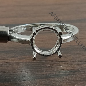 May include: A silver ring setting with a round bezel for a gemstone. The ring is marked with the number "925" indicating it is made of sterling silver.