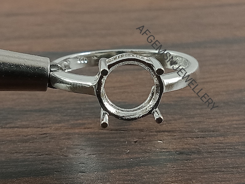 May include: A silver ring setting with a round bezel for a gemstone. The ring is marked with the number "925" indicating it is made of sterling silver.