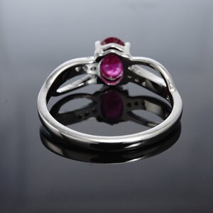 Pode incluir: Um anel de prata com uma gema oval rosa e gemas menores transparentes engastadas na banda.