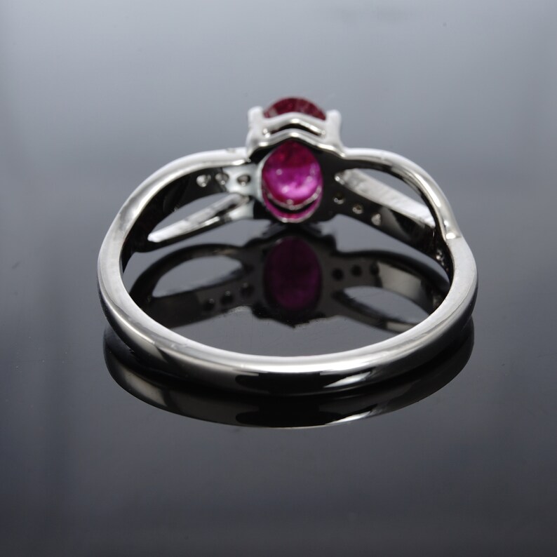 Pode incluir: Um anel de prata com uma gema oval rosa e gemas menores transparentes engastadas na banda.