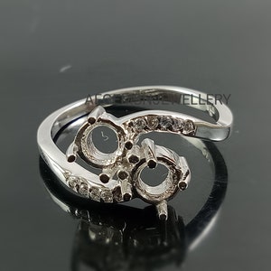 May include: A silver-toned metal ring featuring two empty circular settings for gemstones, accented with small clear stones along the band. The text AFGEMSJEWELLERY is visible on the inner surface of the ring band, which has a polished finish.