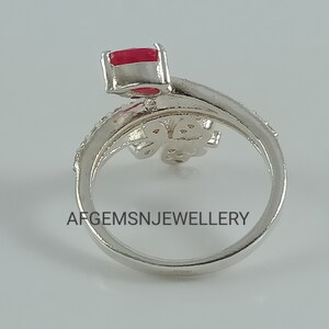 K&ouml;nnte beinhalten: Ein silberner Ring mit einem roten Stein und einem Schmetterlingsdesign. Der Ring liegt auf einem wei&szlig;en Hintergrund. Die Aufschrift 'AFGEMSNJEWELLERY' ist auf dem Ring zu sehen.