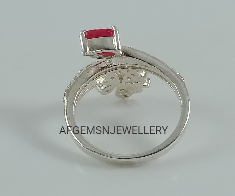 K&ouml;nnte beinhalten: Ein silberner Ring mit einem roten Stein und einem Schmetterlingsdesign. Der Ring liegt auf einem wei&szlig;en Hintergrund. Die Aufschrift 'AFGEMSNJEWELLERY' ist auf dem Ring zu sehen.