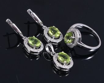 May include: A set of green peridot jewelry featuring a ring, a pendant, and a pair of earrings. Each piece has a silver setting with a halo of small clear stones.