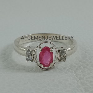 K&ouml;nnte beinhalten: Ein silberner Ring mit einem rosafarbenen ovalen Edelstein, der von einem silbernen Rahmen umgeben ist und auf beiden Seiten zwei kleinere klare Edelsteine hat. Der Ring liegt auf einer wei&szlig;en Oberfl&auml;che. Auf der Ringschiene ist 'AFGEMSNJEWELLERY' eingraviert.