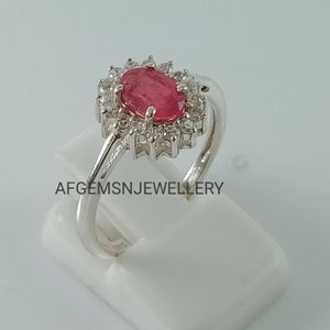 Pu&ograve; includere: Un anello d'argento con una pietra ovale rosa circondata da pietre bianche pi&ugrave; piccole. L'anello &egrave; su un espositore bianco. Il testo 'AFGEMSNJEWELLERY' &egrave; stampato sull'espositore.