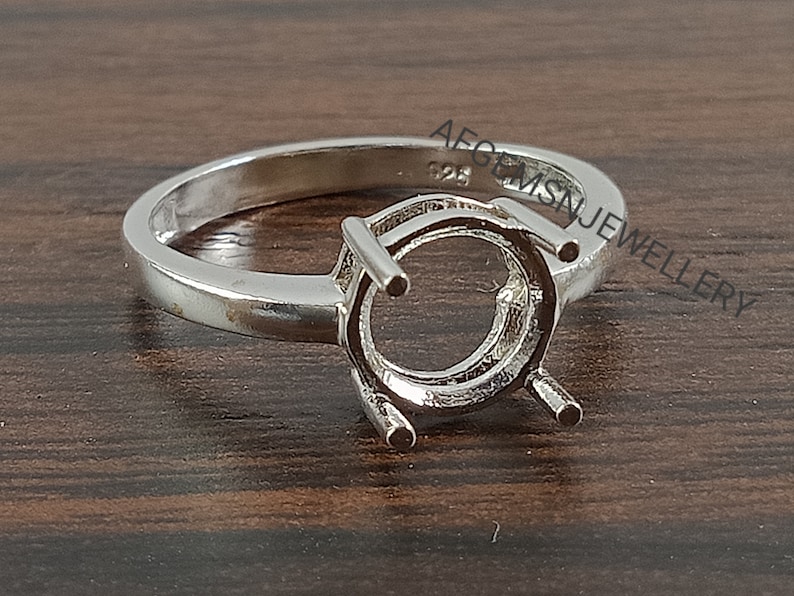 May include: A silver ring setting with a round bezel for a gemstone. The ring is marked "925" on the inside band.
