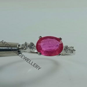 K&ouml;nnte beinhalten: Ein silberner Ring mit einem gro&szlig;en ovalen rosafarbenen Edelstein und kleineren wei&szlig;en Edelsteinen auf der Ringschiene.