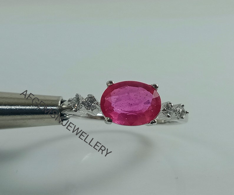 K&ouml;nnte beinhalten: Ein silberner Ring mit einem gro&szlig;en ovalen rosafarbenen Edelstein und kleineren wei&szlig;en Edelsteinen auf der Ringschiene.