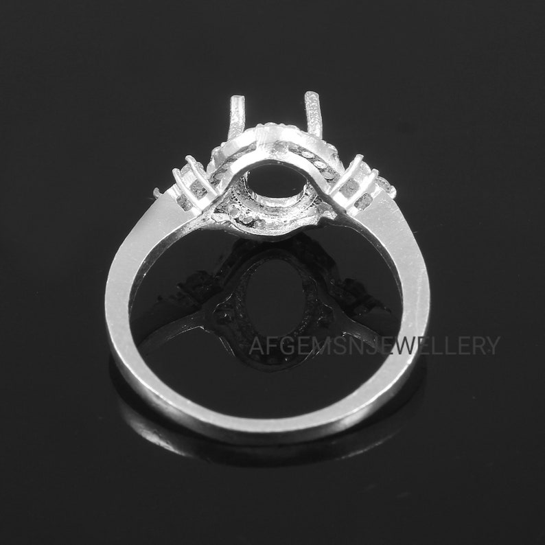 May include: Silver ring setting with a large oval-shaped center stone and smaller accent stones around the band.