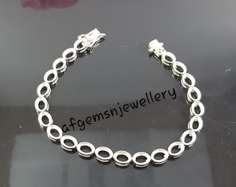 May include: A silver bracelet with oval-shaped settings for stones. The bracelet has a clasp closure.