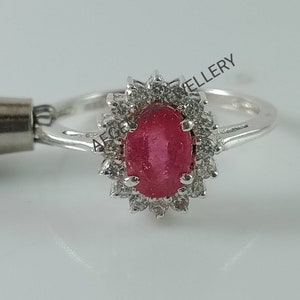 Pu&ograve; includere: Un anello d'argento con un grande rubino ovale circondato da un'aureola di pietre bianche pi&ugrave; piccole.