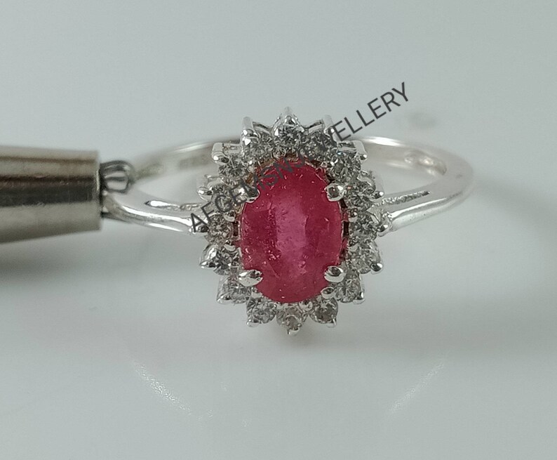 Pu&ograve; includere: Un anello d'argento con un grande rubino ovale circondato da un'aureola di pietre bianche pi&ugrave; piccole.