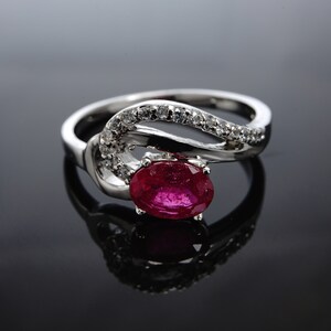 May include: A silver ring featuring a red oval gemstone and a band adorned with small clear gemstones.