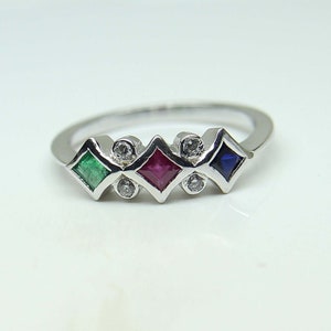 May include: A silver ring with five square-shaped gemstones. The gemstones are emerald green, ruby red, sapphire blue, and two diamonds.